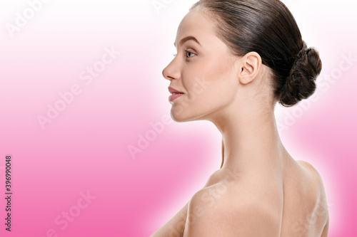 Young woman with perfect healthy skin and hair in bun on a pink background with a shaded white outline