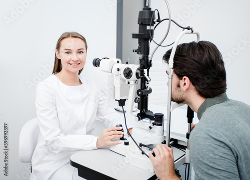 Optometrist woman looking at camera during eye examination of a male patient with special ophthalmic equipment. Ophthalmologist profession