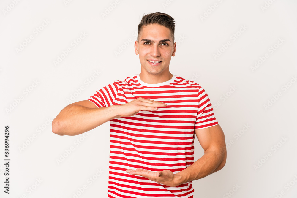 Obraz premium Young caucasian handsome man isolated holding something with both hands, product presentation.