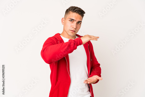 Young caucasian handsome man isolated holding something with both hands, product presentation.
