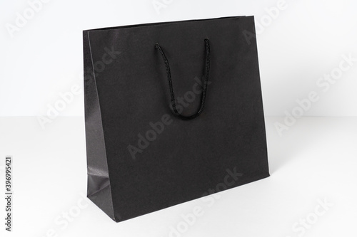 Mockup of black paper shopping bag on neutral grey background.