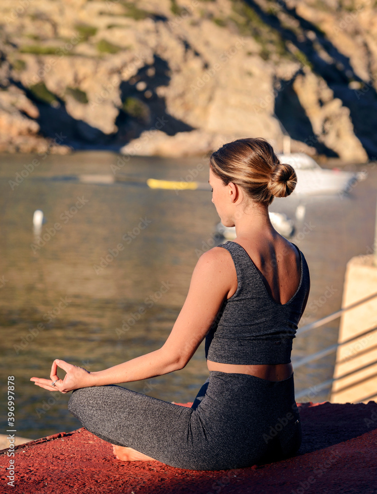 Young fitness woman doing meditation in a lotus yoga pose by the sea.