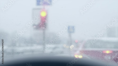 Blurred traffic light background. Rain falling on car windshield view. Traffic light