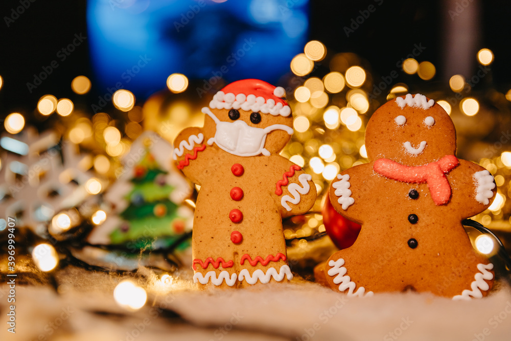 Coronavirus pandemic, conceptual background with unfocused lights christmas decorations and gingerbread in the shape of Santa Claus wearing a protective medical mask