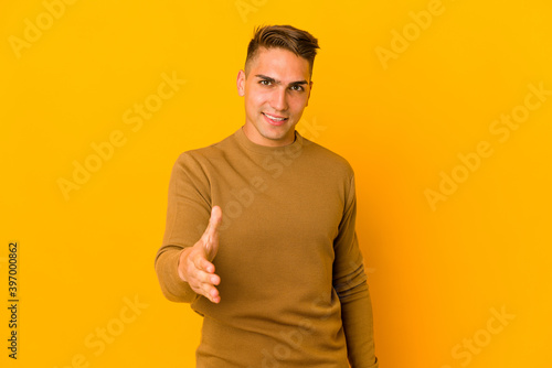 Young handsome caucasian man isolated stretching hand at camera in greeting gesture.