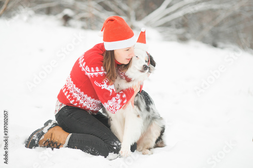 Australian shepherd in santa hat hugging with woman in winter forest 