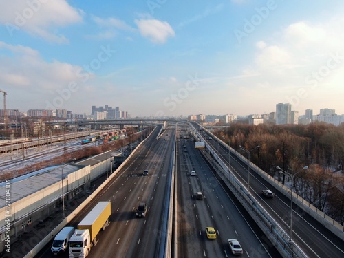 Aerial view flight over a high-speed highway in a big city at dawn. Movement of cars through the streets of the city