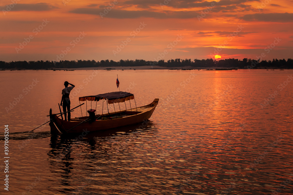DOLPHIN WATCHING, MEKONG RIVER, KRATIE PROVINCE, CAMBODIA - 31 January 2012: Local dolphin watch boat opperator watches beautiful sunset at end of his day. DOLPHIN WATCHING, MEKONG RIVER, KRATIE PROVINCE, CAMBODIA - 31 January 2012: Local dolphin watch boat opperator watches beautiful sunset at end of his day.