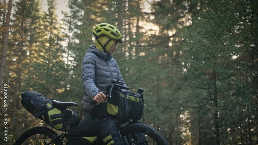 The woman travel on mixed terrain cycle touring with bike bikepacking outdoor. The traveler journey with bicycle bags. Stylish bikepacking, bike, sportswear in green black colors. Magic forest park. The woman travel on mixed terrain cycle touring with bike bikepacking outdoor. The traveler journey with bicycle bags. Stylish bikepacking, bike, sportswear in green black colors. Magic forest park.