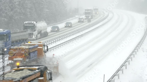 Wide locked down shot of two snow ploughs driving up the highway and clearing the snow off the road in snowfall