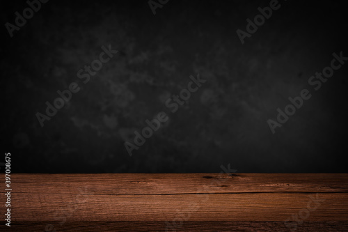 Free space on a wooden table for displaying products with a blurred black wall background.