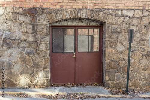 Vintage stone block building with dark red doors and archway on sunny day