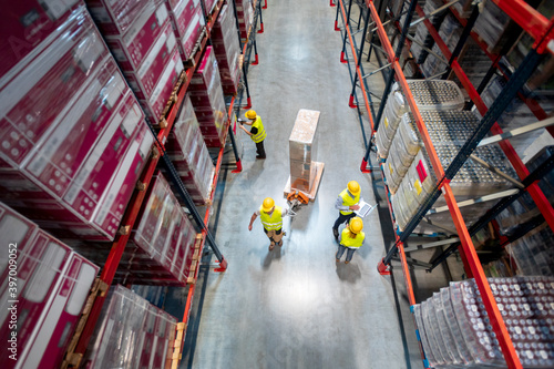 Warehouse workers at work between rows of tall shelves full of packed boxes, top view photo