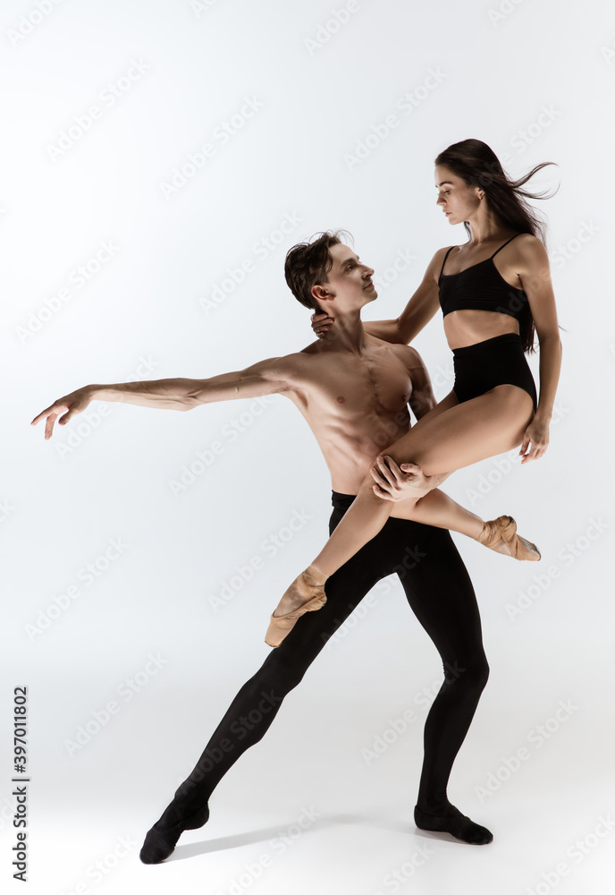 Fototapeta premium Young and graceful ballet dancers in minimal black style isolated on white studio background. Art, action, flexibility, inspiration, lightness of the body concept. Flexible caucasian ballet dancers.