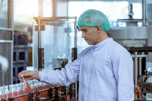 Worker of science in bottle beverage factory wearing safety  hat and face mask working to check quality of drink Basil seed produce on conveyer belt before distribution to market business.