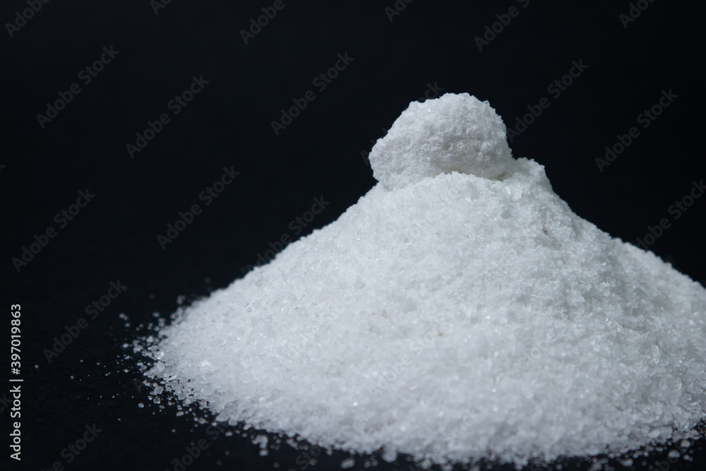 A pile of salt on a black background, a piece of salt lies on top. Excessive salt intake. Coarse salt A pile of salt on a black background, a piece of salt lies on top. Excessive salt intake. Coarse salt