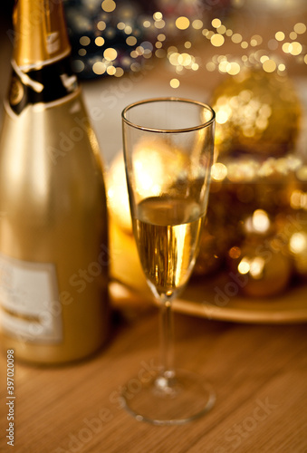 Christmas table setting with holiday decorations in a gold color. New Year celebration. A bottle and glass of champagne.