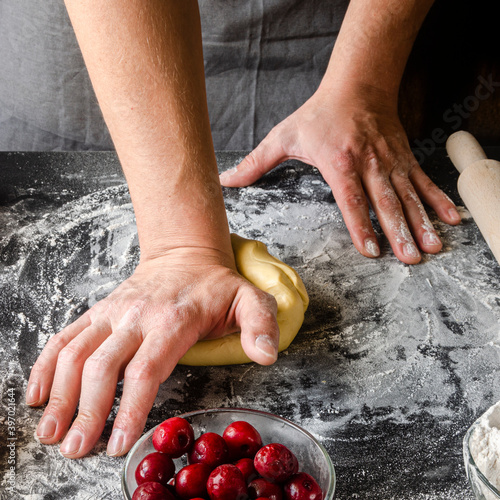 The man's hands knead the dough for the preparation of cherry strudel