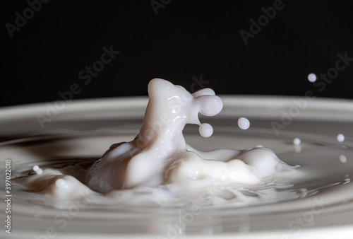 Milk in a bowl, with red tinged milk dropping to collide.