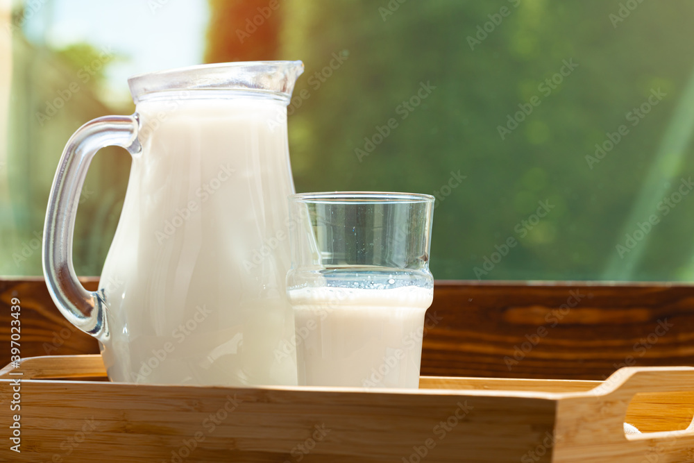 Pitcher of milk on wooden table against blurred foliage background Pitcher of milk on wooden table against blurred foliage background