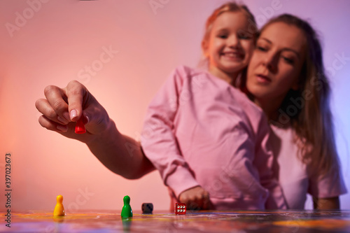 Board game concept - your move. Little girl watched the game and shock from the action move. Board game field, many figures. Kid girl play in board game at home on red blue neon light background