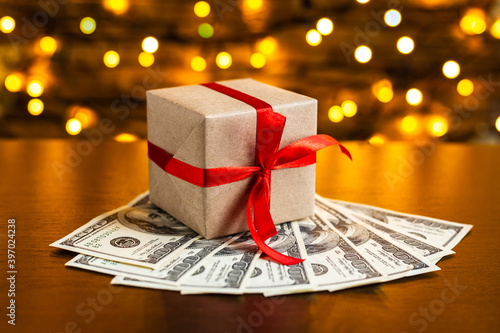 Gift box on the pile of USA 100 dollar bills on blurred lights background. American dollar. Christmas and New Year money present. Gift cost. Hundred. Finance and business concept. Christmas shopping