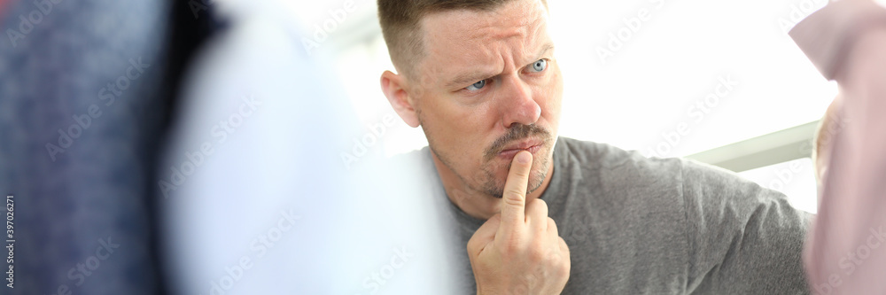 Pensive man looks at hanger with clothes. Men's wardrobe and stylish clothing concept Pensive man looks at hanger with clothes. Men's wardrobe and stylish clothing concept