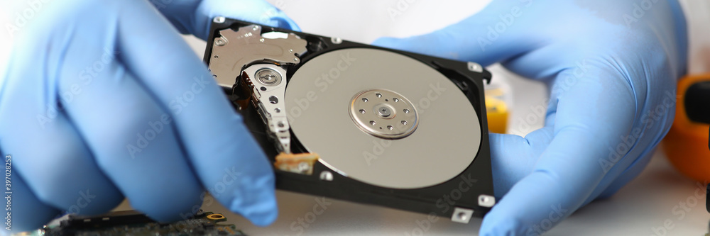 Gloved master holds hard drive away from computer. Computer repair service concept Gloved master holds hard drive away from computer. Computer repair service concept