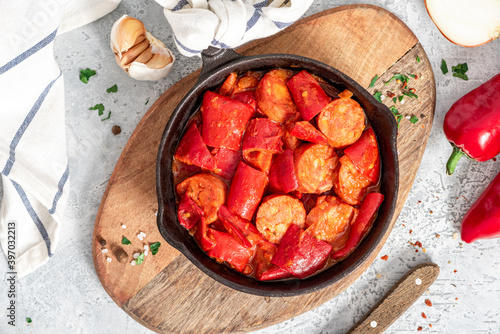 Sausages stewed with peppers, onions and tomatoes in a pan on a gray concrete background. Traditional Hungarian food lecho with sausages and vegetables.