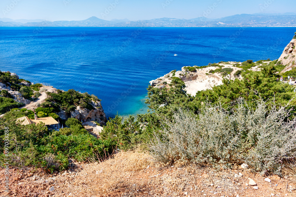 A hard, thorny shrub grows on the slope of the Gulf of Corinth against the backdrop of a blue lagoon on the coast.