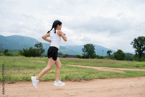 Happy Funny little asian girl fitness woman running at morning tropical forest trail. Athletic young child running in the nature. Healthy lifestyle.