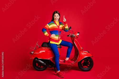 Photo portrait of smart girl having idea raising finger up sitting on scooter isolated on vivid red colored background
