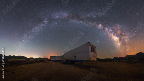 night panorama of the arch of the milky way over the trailer of an abandoned truck in the desert