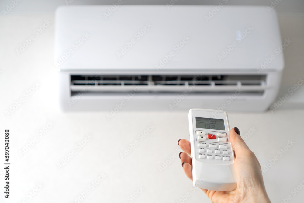 Fototapeta premium Room air conditioning. Air conditioner remote control in female hands. Copy space.