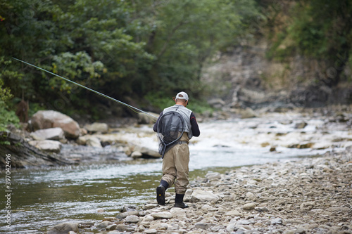 Back view of fisherman walking along mountain river with rod