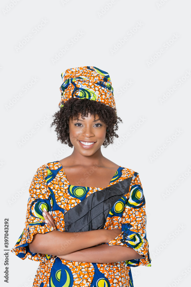 Portrait of young woman in African print attire standing arms crossed over gray background Portrait of young woman in African print attire standing arms crossed over gray background