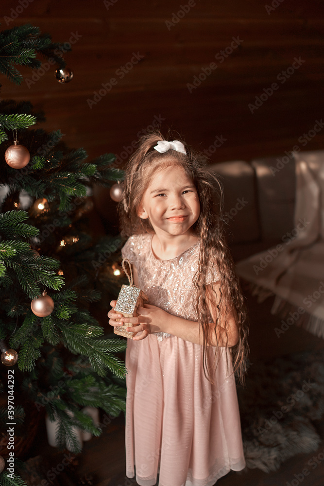 Adorable little toddler girl with curly hair in a warm knitted dress decorating a beautiful Christmas tree at a big window with a view of a snowy garden Adorable little toddler girl with curly hair in a warm knitted dress decorating a beautiful Christmas tree at a big window with a view of a snowy garden