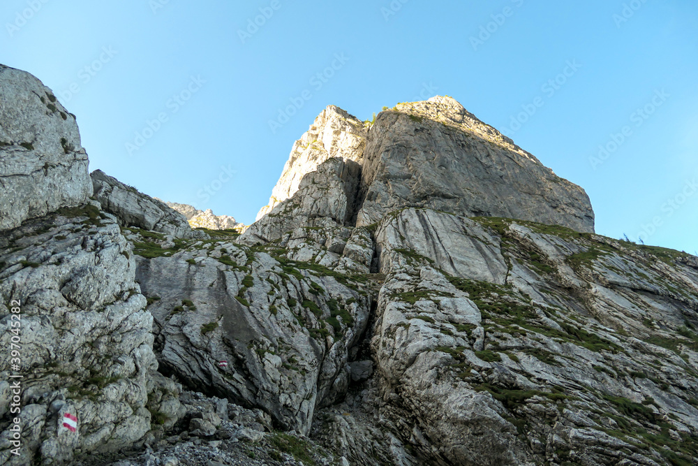 A steep mountain wall on the way to Grimming in Austrian Alps. Dangerous climbing only for professionals. The sky above it is blue, one small cloud. Extreme sport. red path mark on the side. A steep mountain wall on the way to Grimming in Austrian Alps. Dangerous climbing only for professionals. The sky above it is blue, one small cloud. Extreme sport. red path mark on the side.