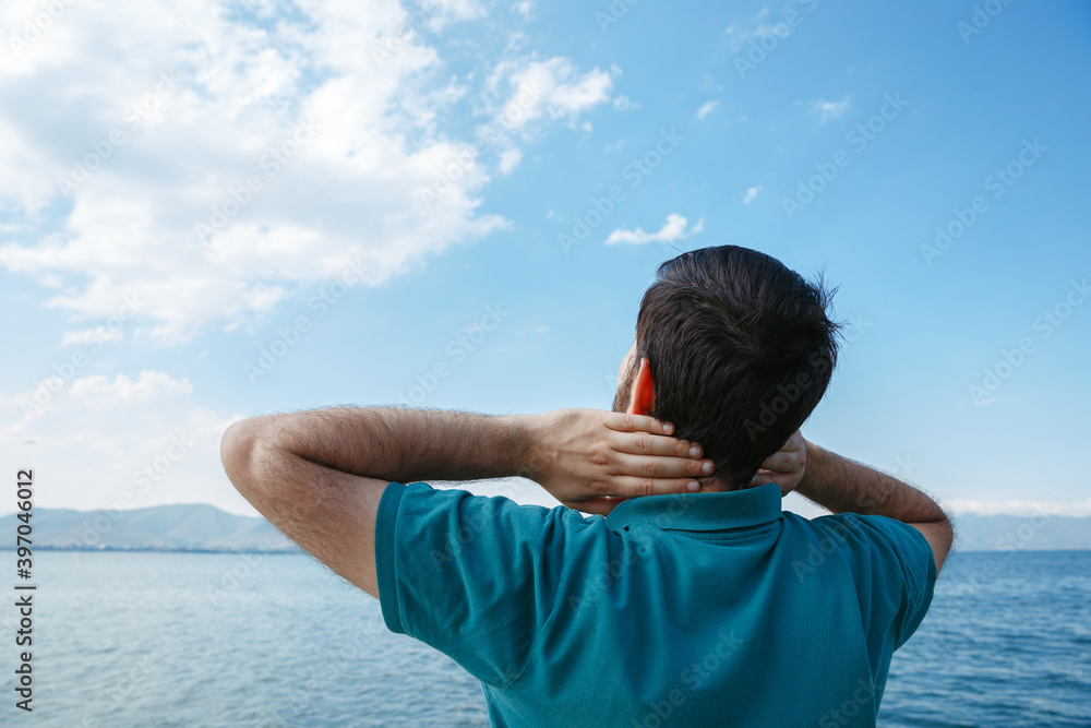 Carefree male tourist standing with hands behind head and enjoying freedom and summer vacation near sea Carefree male tourist standing with hands behind head and enjoying freedom and summer vacation near sea