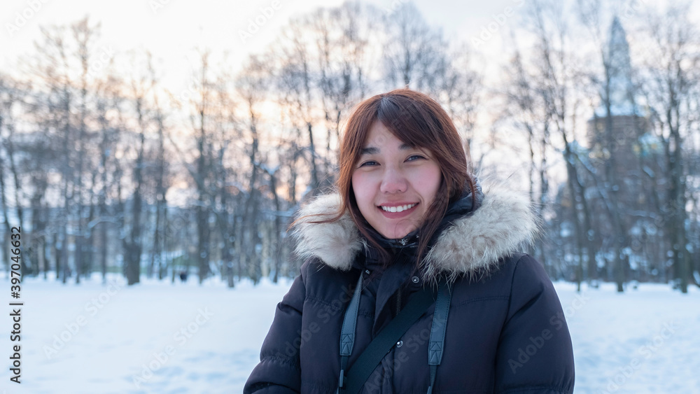 Woman traveler asian female in warm black winter outfit with light brown fur smile under sunlight with snow and forest background. Thai lady tourist in cold country nature outdoor hiking activity. Woman traveler asian female in warm black winter outfit with light brown fur smile under sunlight with snow and forest background. Thai lady tourist in cold country nature outdoor hiking activity.