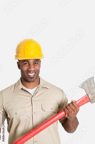 Portrait of happy African male construction worker holding axe over gray background