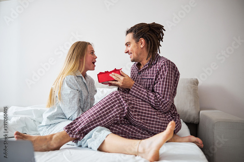 Cheerful man giving present to happy girlfriend in bedroom