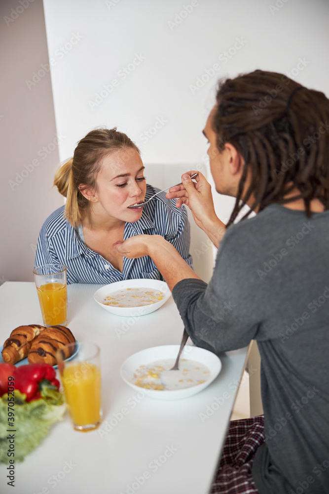 Loving young man feeding girlfriend with spoon in kitchen Loving young man feeding girlfriend with spoon in kitchen