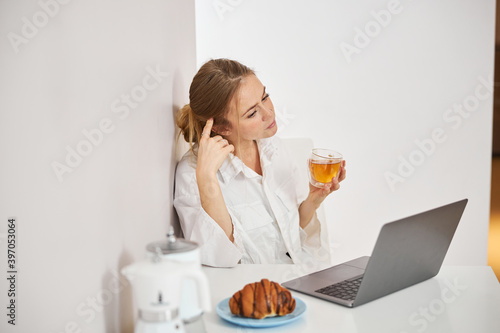 Charming young woman drinking tea and using laptop at home