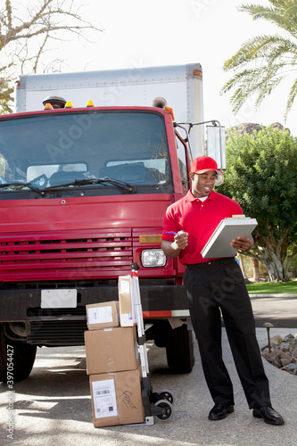 Young delivery man looking at delivery list on clipboard with truck in background