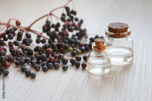elderberry essential oil (tincture, extract, infusion) with fresh elderberry on wooden background