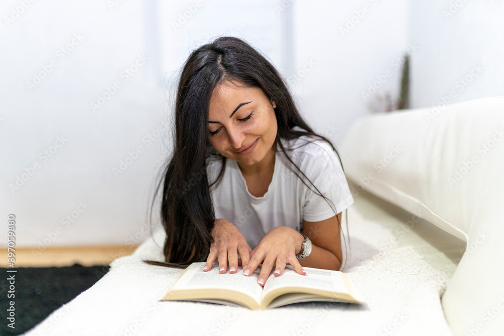 Young beautiful woman lying on bed while reading book Young beautiful woman lying on bed while reading book