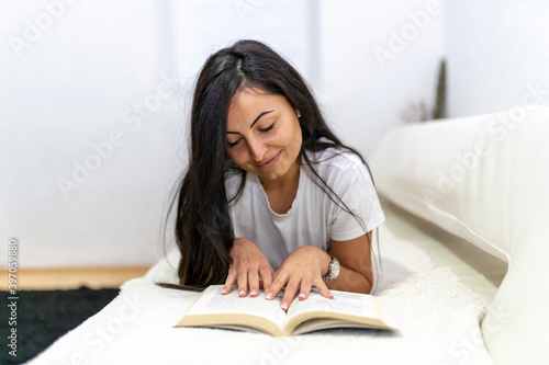 Young beautiful woman lying on bed while reading book