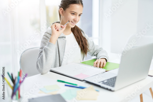 Online class. Cheerful latin teenage girl smiling, looking at the laptop screen while communicating with her teacher, having online lesson at home
