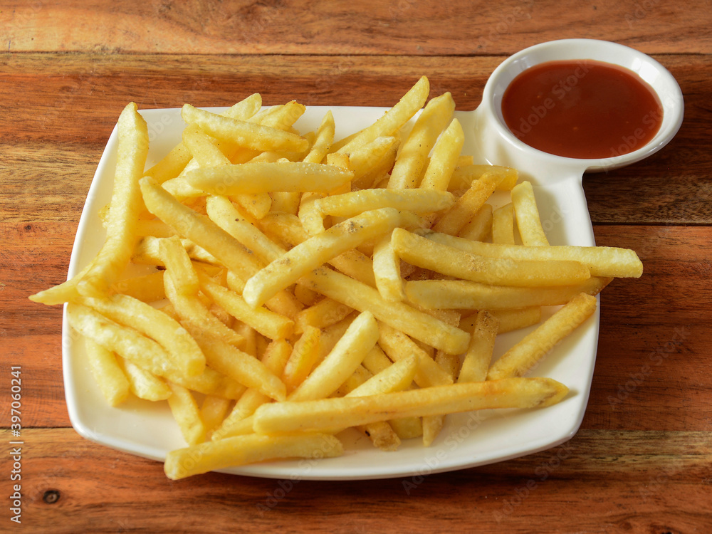 Golden fried French fries served in a plate with tomato ketchup over a rustic wooden background, selective focus Golden fried French fries served in a plate with tomato ketchup over a rustic wooden background, selective focus